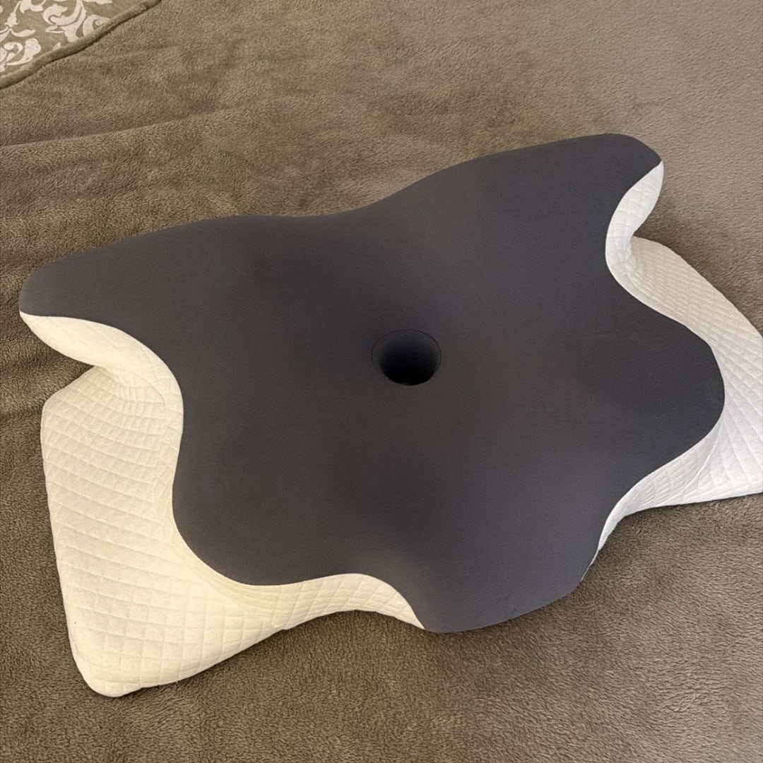 Oreiller ergonomique gris foncé posé sur un lit