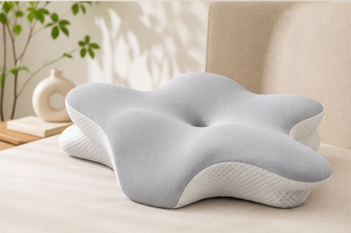 Oreiller ergonomique gris clair posé sur un lit, vu de trois quarts