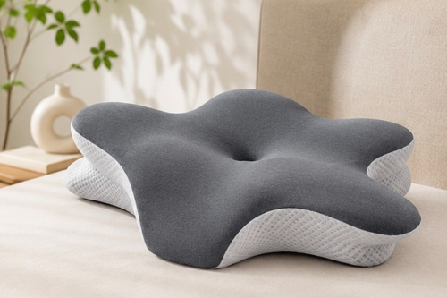 Oreiller ergonomique gris foncé posé sur un lit, vu de trois quarts